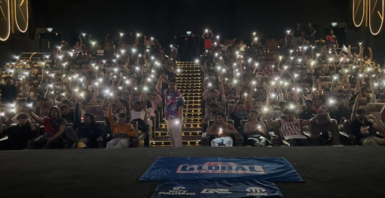 A packed cinema hall lit by hundreds of phone torches during a GE watch party