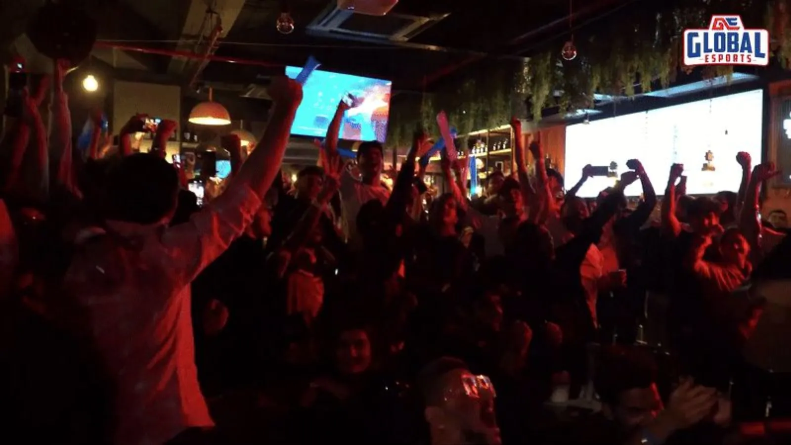 Fans with arms raised in a bar watching GE play