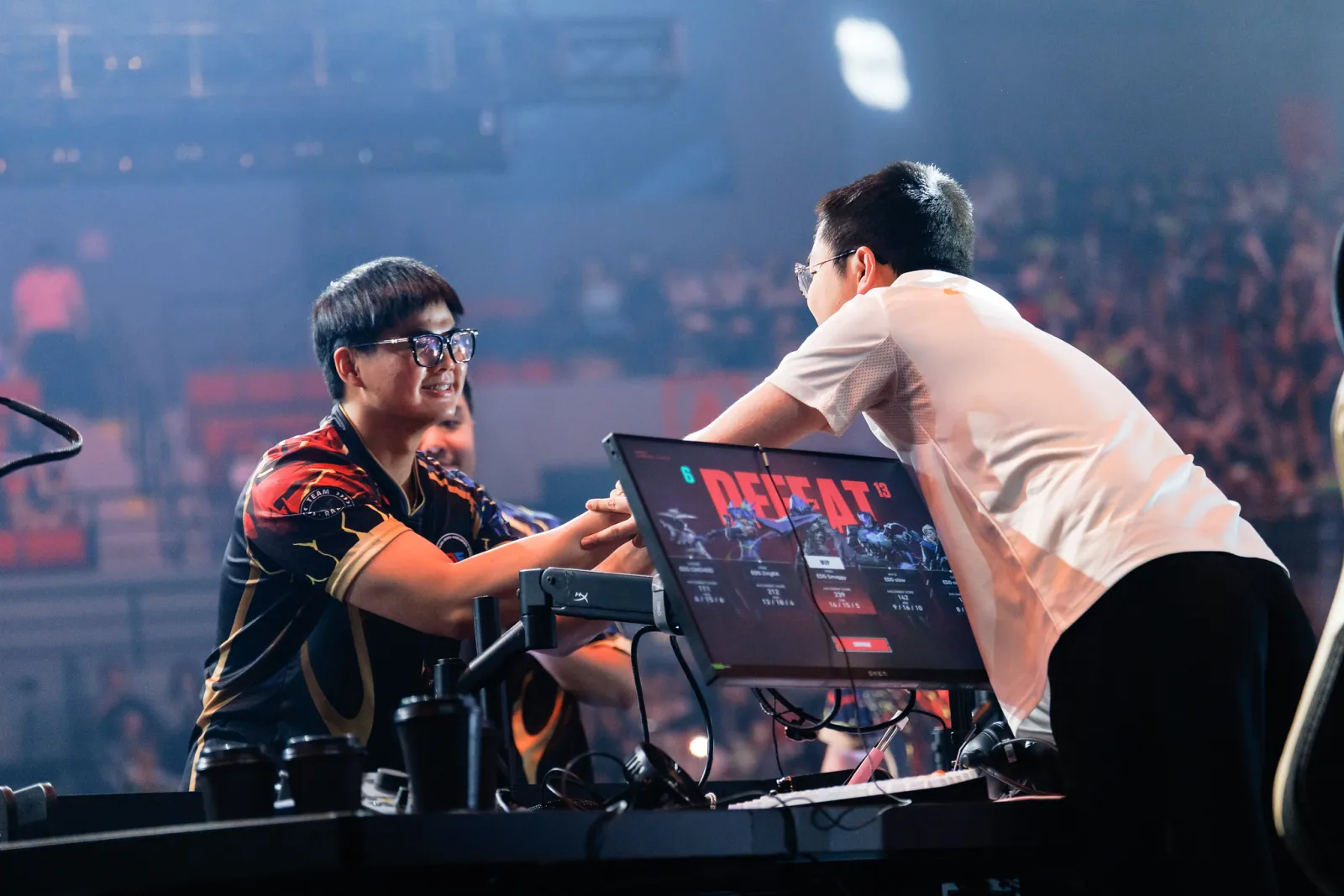 PatMen of Global Esports smiles as he shakes hands with ZmjjKK of EDward Gaming over a screen reading DEFEAT